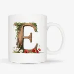Witte mok met een opdruk van een houten letter E met klaprozen, bloemen en klimop.