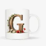Witte mok met een opdruk van een houten letter G met klaprozen, bloemen en klimop.