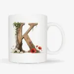 Witte mok met een opdruk van een houten letter K met klaprozen, bloemen en klimop.